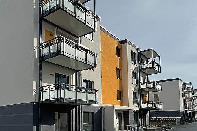 Moderne Mehrfamilienhäuser der Erlenhöfe in Jena mit Balkonen sowie weißen, grauen und gelben Fassaden.