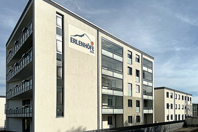 Mehrfamilienhaus im Wohnquartier Erlenhöfe Jena mit verglasten Balkonen und Erlenhöfe-Schriftzug an der Fassade.