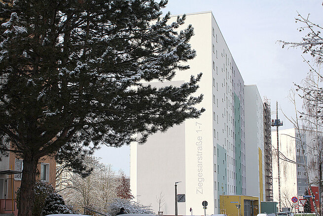 Modernisiertes mehrgeschossiges Wohngebäude der WG Carl Zeiss in Jena mit heller Fassade und farbigen Fassadenelementen im Winter.