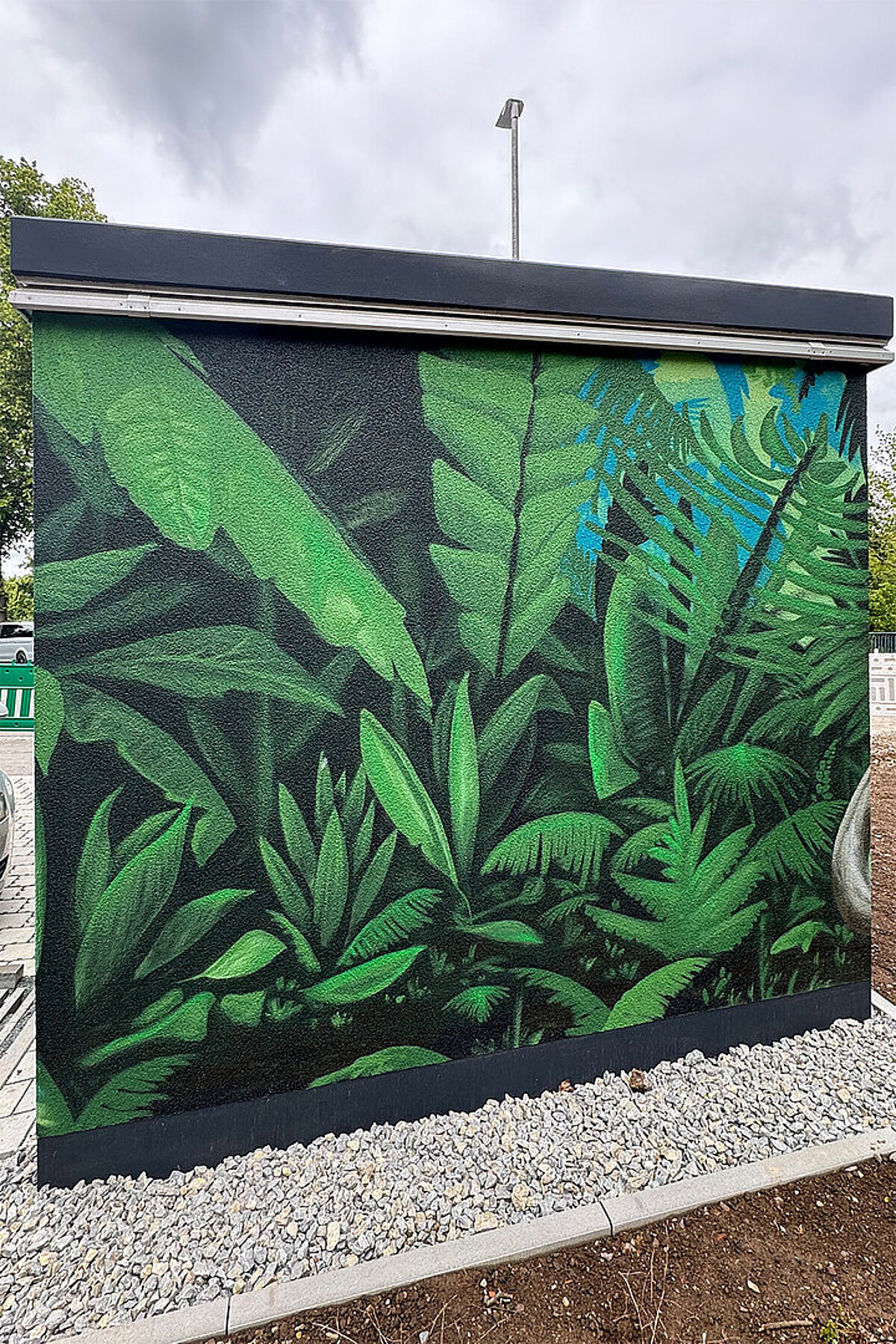 Technikgebäude in den Erlenhöfen Jena mit großflächiger grüner Fassadenkunst aus tropischen Pflanzenmotiven.